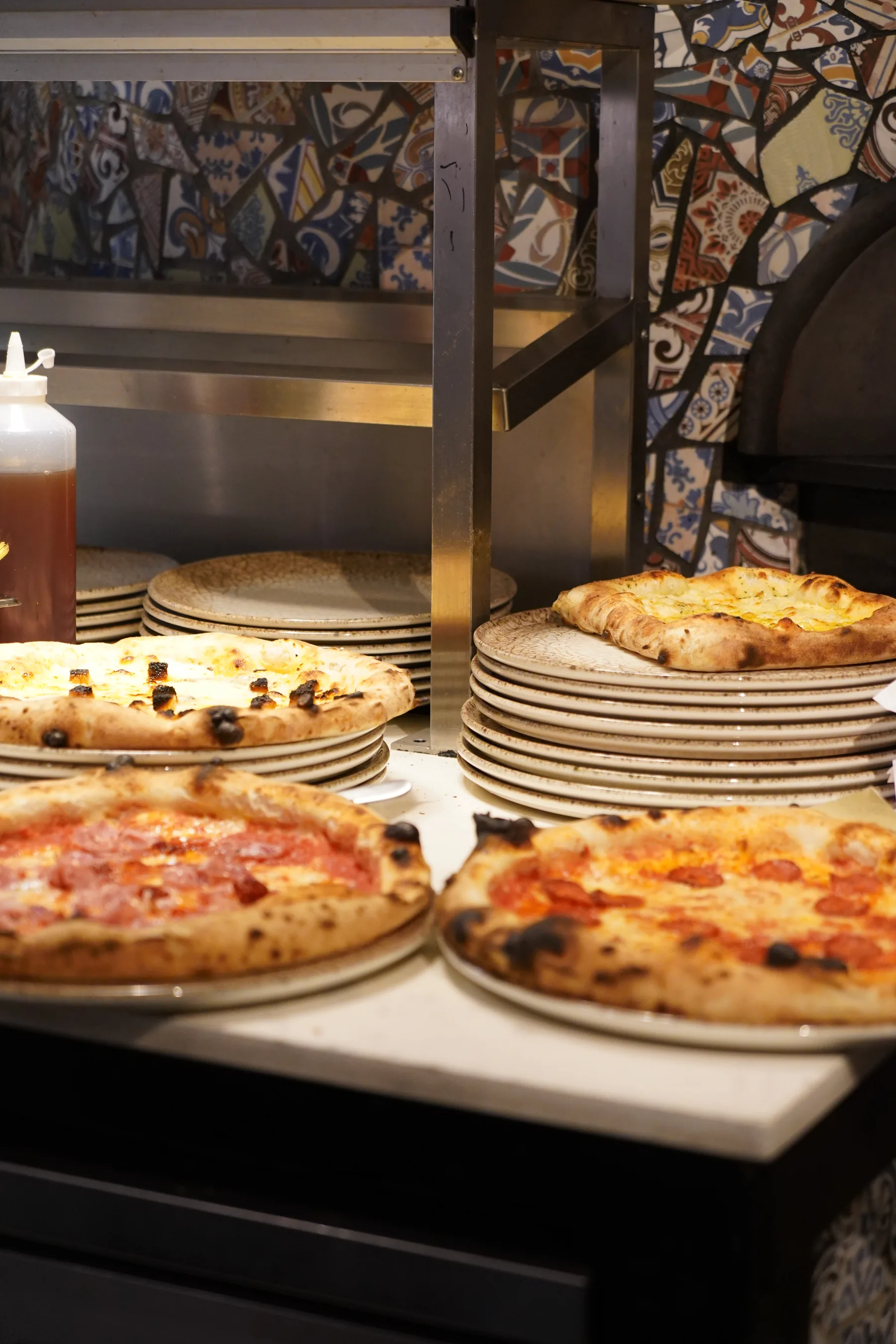 A counter full of just-out-of-the-oven pizzas beside the mosaic-tiled wood-fired oven